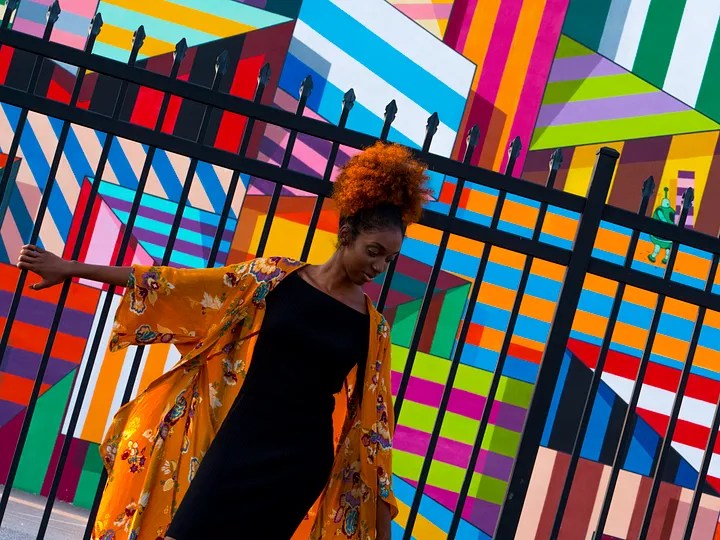 Woman in yellow coat standing in front on abstract coloured wall