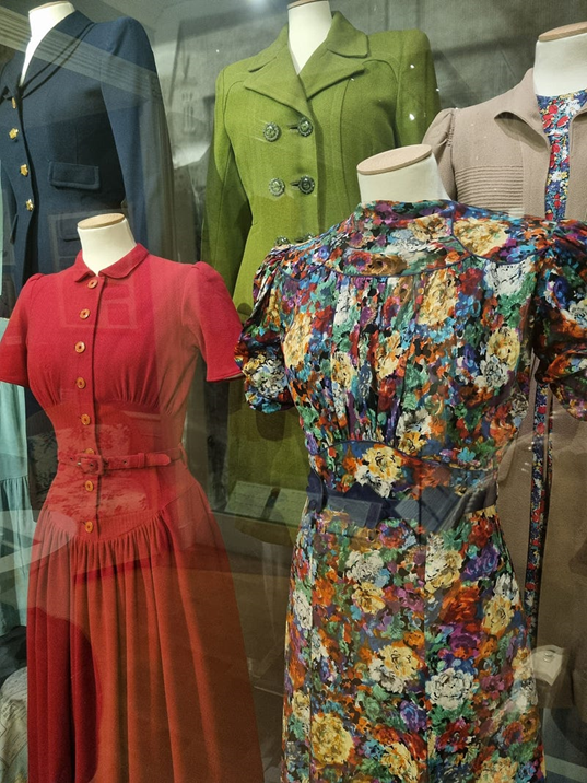 Collection of three items — red dress with belt and collar, print dress with short sleeves and green tailored jacket with Bakelite buttons.