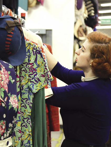 Auburn haired woman in dark blue dress looking through clothes rail