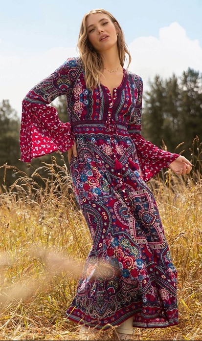 Blonde girl waling in long grass wearing dark red and blue patterned boho dress