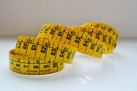 Yellow tape measure with black writing losely wound up, showing centimeters